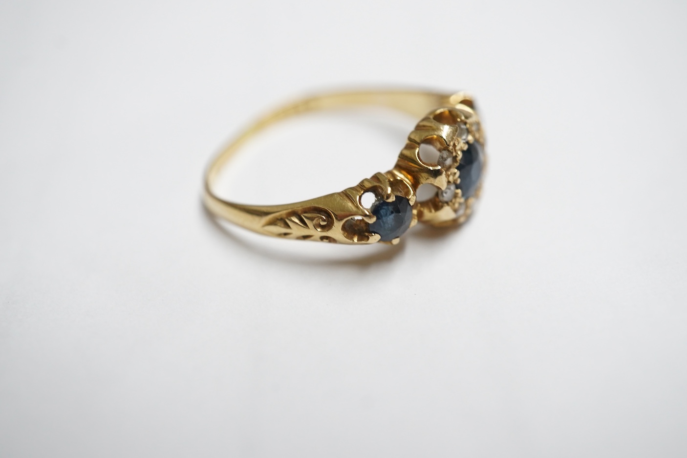 An early 20th century yellow metal and three stone sapphire set half hoop ring, the central stone bordered with rose cut diamonds, size M, gross weight 3 grams.